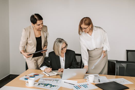Three businesswomen discussing documents during a meeting in a modern office setting.